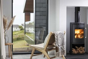 Ein modernes Interieur mit einer Glastür, die auf einen Balkon führt, einem Holzschaukelstuhl mit gemustertem Überwurf und einem schwarzen Kaminofen.
