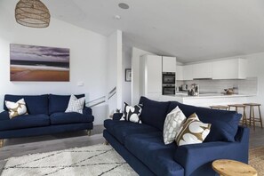 Ein modernes Wohnzimmer mit einer Sofagarnitur, einem Teppich und einer Küche im Hintergrund.