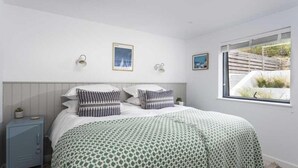 Ein Schlafzimmer mit einem Bett, einem Nachttisch, Wandlampen und einem Fenster mit Blick.