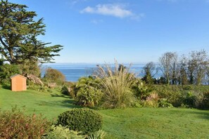 A grassy landscape with a small wooden shed, dense shrubbery, and a view of the ocean. - 2 Bed in Carbis Bay (oc-b584272) (Carbis Bay)