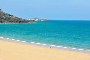 A beach with clear blue water, a sandy shore, and a distant hill with buildings. - 2 Bed in Carbis Bay (oc-b584272) (Carbis Bay)