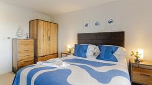 A bedroom with a bed, a wardrobe, bedside tables, and wall art. - 4 Bed in Holywell Bay (oc-b659846) (Holywell)