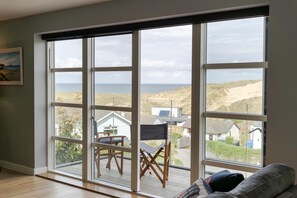 Ein Zimmer mit großen Fenstern, Holzboden und Blick auf das Meer und Häuser.