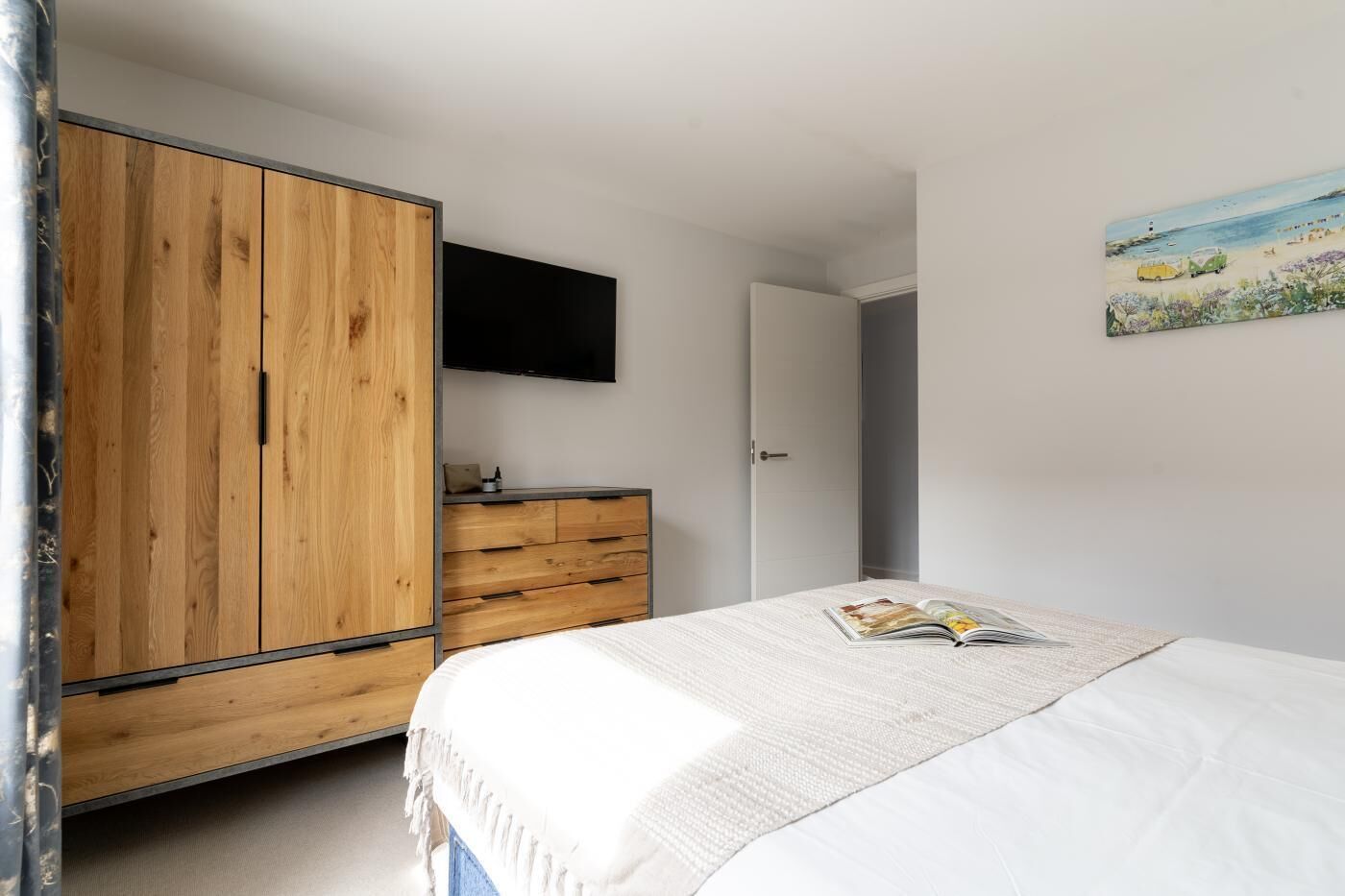 Un dormitorio con cama, un armario de madera, un televisor y un cuadro en la pared.