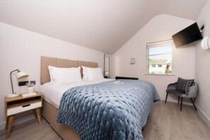 A bedroom with a bed, bedside table, lamp, chair, and a mounted TV. - 4 Bed in Porth (oc-b588791) (Newquay)