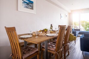 A dining area with a wooden table set for four, surrounded by wooden chairs with cushioned seats. - 4 Bed in Porth (oc-b588791) (Newquay)