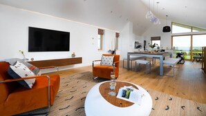 Ett modernt vardagsrum med en platt-TV, en orange soffa och en matplats med bord och stolar.