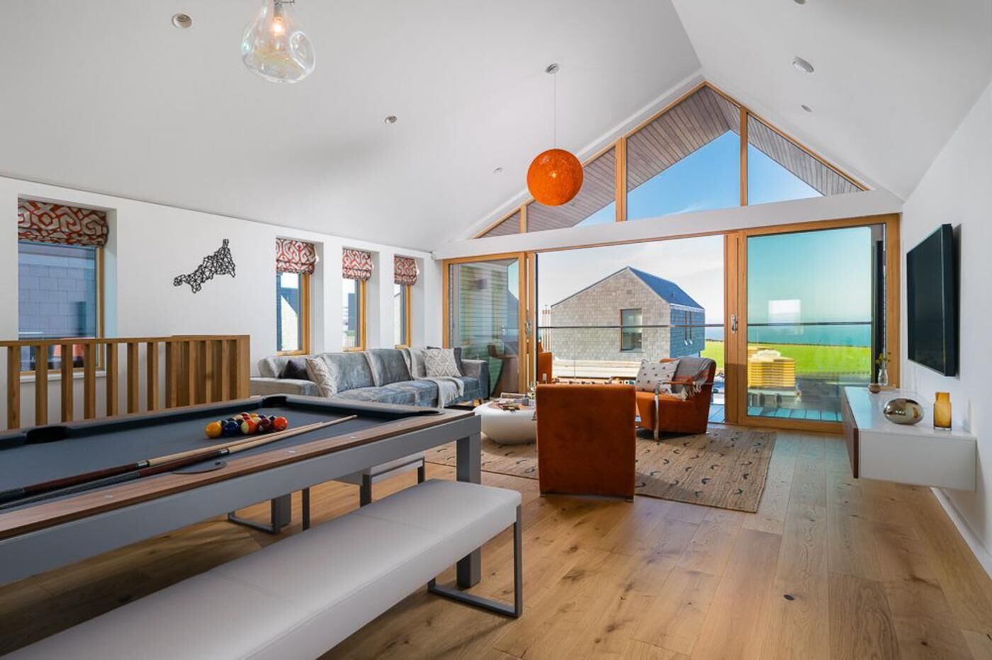 A modern living room with a pool table, seating area, and large windows offering a view of the outdoors.