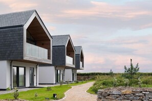 A modern two-story building with a symmetrical design, featuring large windows and a gravel pathway leading to the entrance. - 3 Bed in St. Eval (oc-b584290) (Saint Eval)