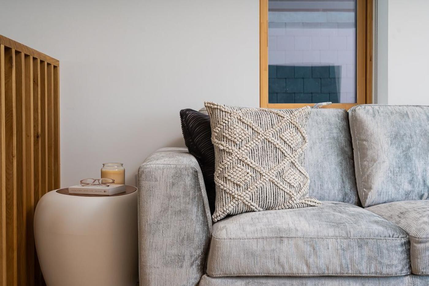 A modern living room with a grey sofa, a round side table, and a window with a view of a brick building.