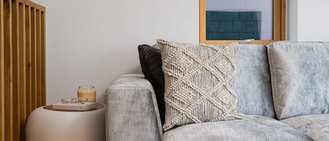 A modern living room with a grey sofa, a round side table, and a window with a view of a brick building.