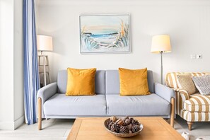 Ein Wohnzimmer mit einer Couch, zwei Lampen, einem Gemälde und einem Couchtisch mit einer Zapfen-Schale.