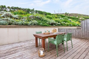 Eine Holzterrasse mit Tisch und Stühlen, umgeben von einem üppigen Garten und einem Holzzaun.