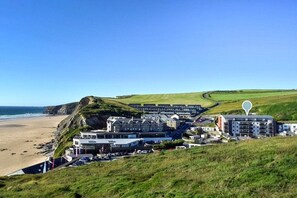 Ein Küstenhotel mit mehreren Gebäuden, einem Strand und einer hügeligen Landschaft.