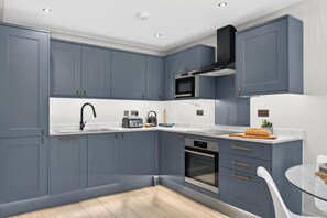 A modern kitchen with grey cabinetry, a stainless steel oven, and a microwave. - 2 Bed in Watergate Bay (oc-b598859) (Tregurrian)