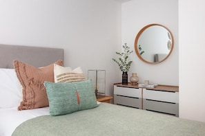 Ein Schlafzimmer mit Bett, Kissen, Nachttisch, Spiegel und Kommode.