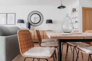 Uma sala de jantar moderna com uma mesa de madeira, cadeiras de vime com almofadas brancas e um arranjo de flores em um vaso de vidro.
