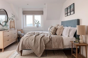 Ein Schlafzimmer mit Bett, Nachttisch, Kommode, Fenster und Blick ins Freie.