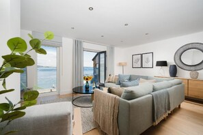 Uma sala de estar moderna com um sofá cinzento, uma mesa de centro e vista para o mar.