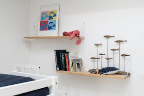 Ein Zimmer mit einem weißen Bett, einem Regal mit Büchern und einem Stofftier, sowie einer an der Wand befestigten Fischdekoration.