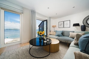 A modern living room with a large window, a round coffee table, a sofa, and a view of the sea.