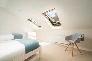 Une chambre avec un plafond en pente, deux fenêtres de toit, un lit, une chaise et un radiateur.