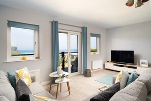 A modern living room with a large TV, comfortable seating, and a view of the sea. - 3 Bed in Mawgan Porth (oc-b584450) (Mawgan Porth)