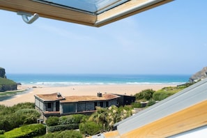 A beachfront property with a modern house, a clear view of the ocean, and a rocky cliff. - 3 Bed in Mawgan Porth (oc-b584450) (Mawgan Porth)