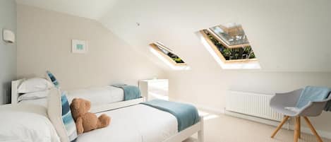A bedroom with a sloped ceiling, two skylights, a bed with pillows, a chair, and a radiator.