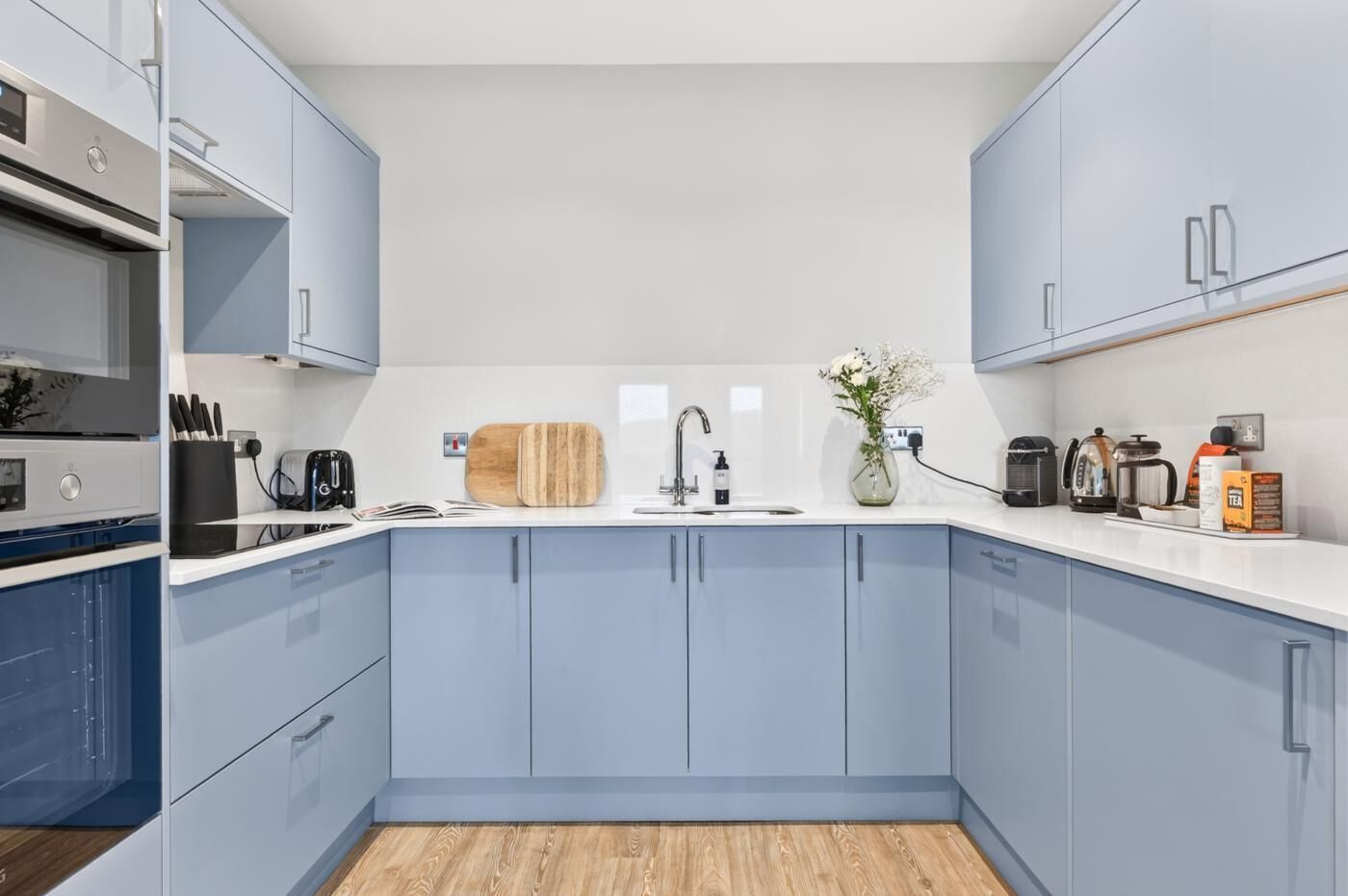 A modern kitchen with grey cabinets, a white countertop, and a wooden floor.