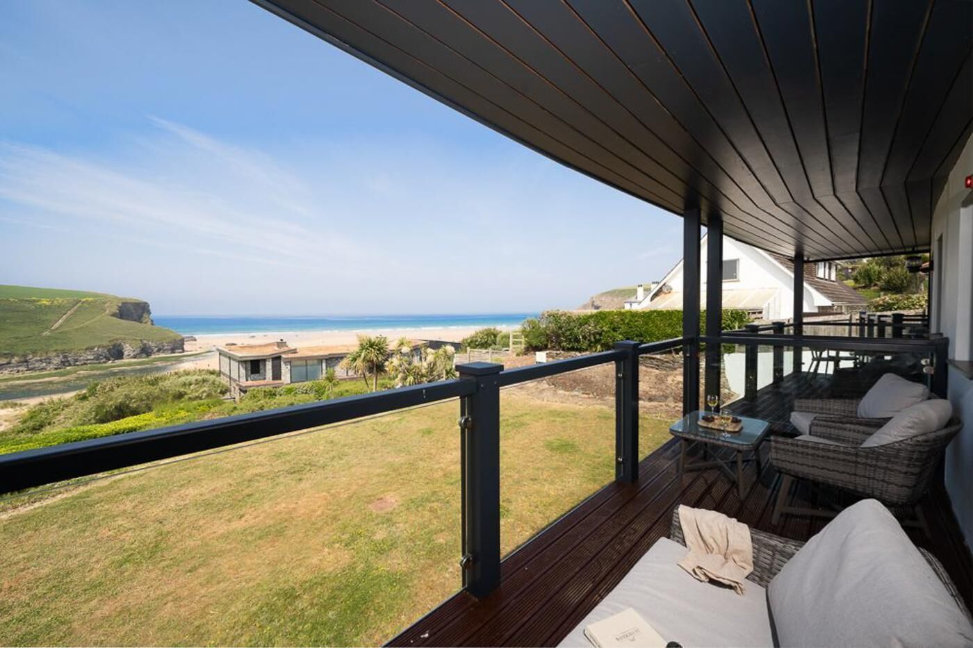 Ein Balkon mit Blick auf Strand und Meer, ausgestattet mit Sitzgelegenheiten und Kissen sowie einem Tisch mit einem Glas.