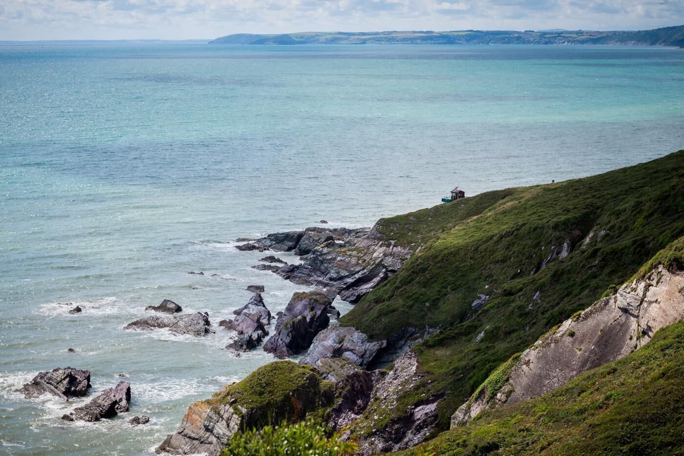 Eine Küstenlandschaft mit felsigen Klippen und einer grasbewachsenen Böschung mit Blick auf das Meer.