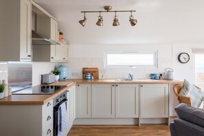 A modern kitchen with white cabinets, a wooden countertop, a built-in oven, a kettle, and a window above the sink. - 2 Bed in Whitsand Bay (oc-b584334) (Freathy)