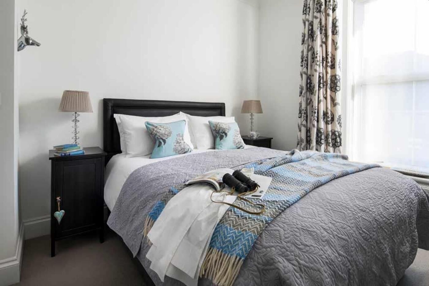 A neatly made bed with a patterned bedspread, two bedside tables with lamps, and a window with curtains.