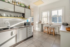 Une cuisine moderne équipée d’un four encastré, d’un four à micro-ondes et d’un évier. On y trouve des tabourets au comptoir et une fenêtre donnant sur l’extérieur.