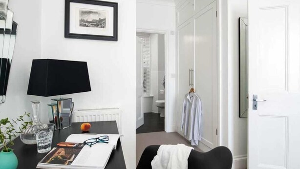 A hotel room with a desk, a framed picture, a radiator, a mirror, a potted plant, and a door leading to a bathroom. - 4 Bed in Fowey (oc-b584335) (Fowey)