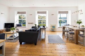 A spacious living area with a sofa, a dining table, and a TV. - 4 Bed in Fowey (oc-b584335) (Fowey)