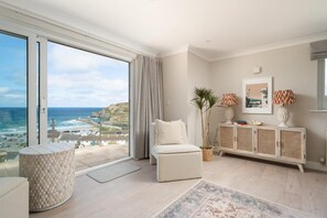 Ein geräumiges Wohnzimmer mit einem großen Fenster mit Meerblick, einem weißen Sofa, einem gemusterten Teppich und einem dekorativen Schrank.