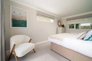Ein Schlafzimmer mit Bett, Stuhl, Nachttisch, Fenster und einem Bild an der Wand.