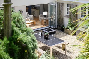 A modern outdoor living area with a patio table, seating, and a glass door leading to an interior space. - 5 Bed in Mawgan Porth (oc-b621974) (Mawgan Porth)