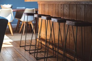A row of bar stools with metal legs and wooden seats, positioned against a wooden wall in a dining area with a wooden floor. - 5 Bed in Mawgan Porth (oc-b621974) (Mawgan Porth)
