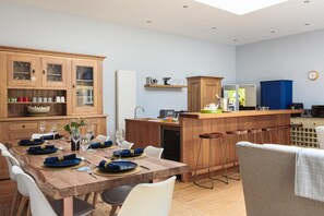 A modern kitchen with wooden cabinetry, a dining table set for six, and a bar area. - 5 Bed in Mawgan Porth (oc-b621974) (Mawgan Porth)
