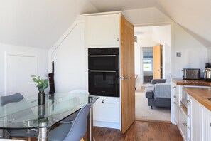 A compact kitchen with a glass dining table and chairs, a built-in oven, and a wooden countertop. - 5 Bed in Mawgan Porth (oc-b621974) (Mawgan Porth)