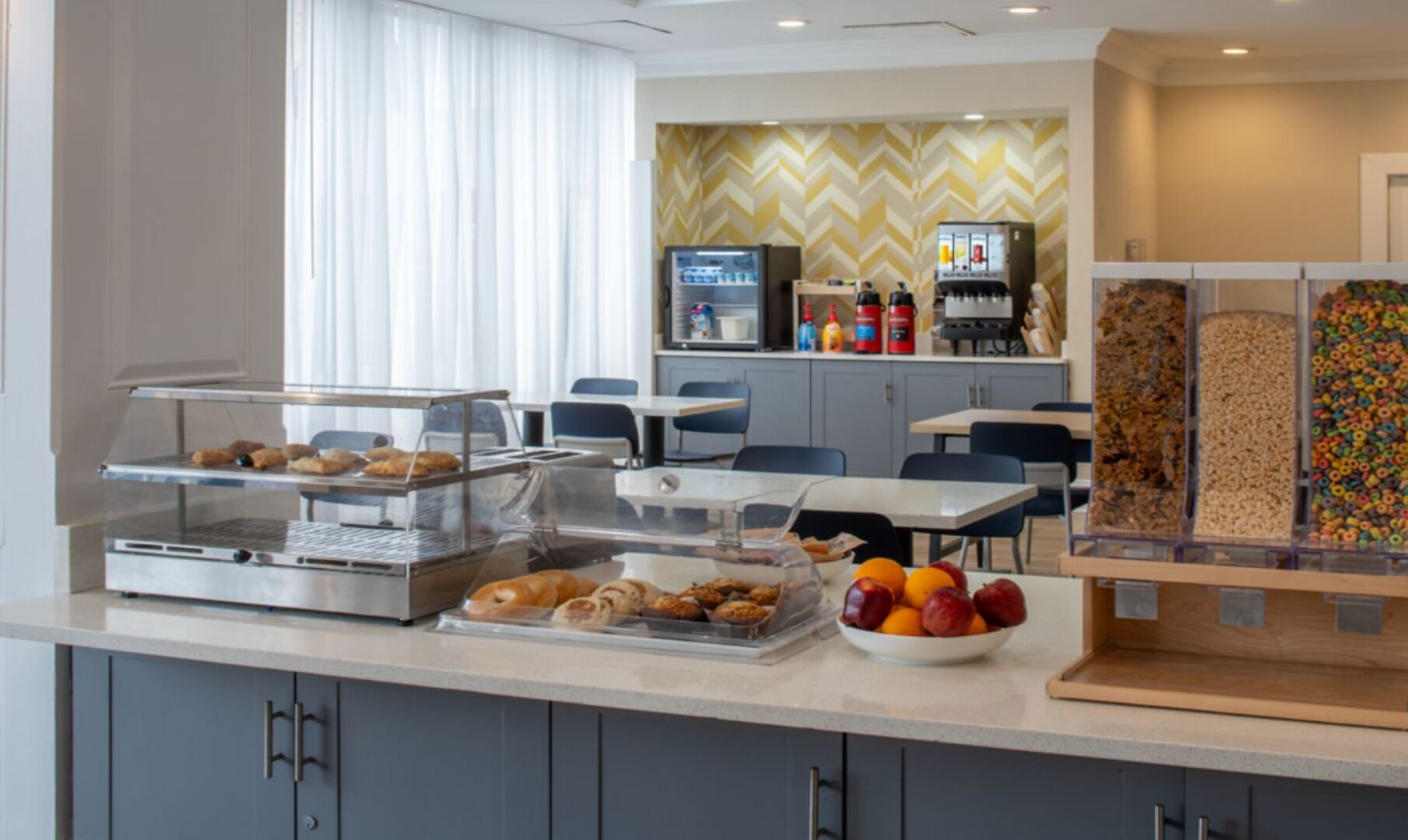 A hotel breakfast area with a self-service station, seating, and a vending machine.