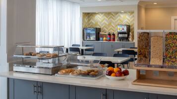 A hotel breakfast area with a self-service station, seating, and a vending machine.