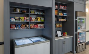 Una kitchenette con estantes llenos de refrigerios, un refrigerador y un congelador.