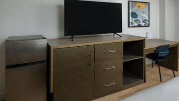 A compact room with a desk, a flat-screen TV, a VISSANI refrigerator, and a chair.