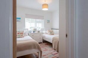Een slaapkamer met twee bedden, een nachtkastje, een lamp en een raam met jaloezieën.