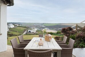 A wicker table with four chairs on a patio overlooking a scenic landscape. - 4 Bed in Mawgan Porth (oc-b650080) (Mawgan Porth)