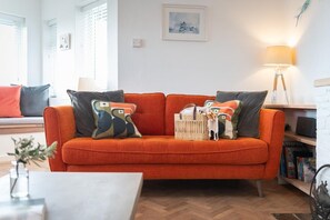 Ein Wohnzimmer mit einer Couch, Kissen, einer Lampe und einem Bücherregal.